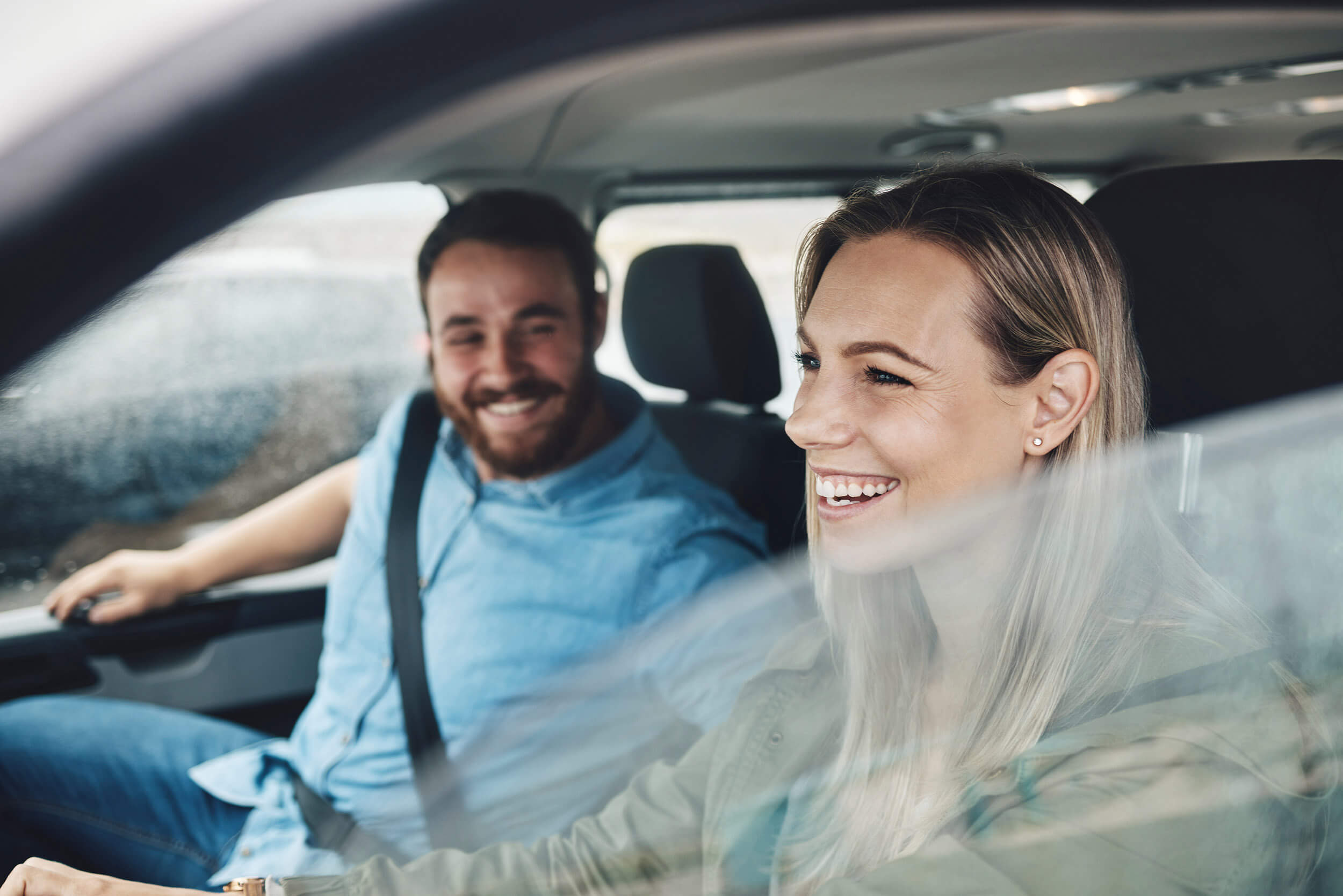 Pareja sonriendo mientras conduce su auto asegurado